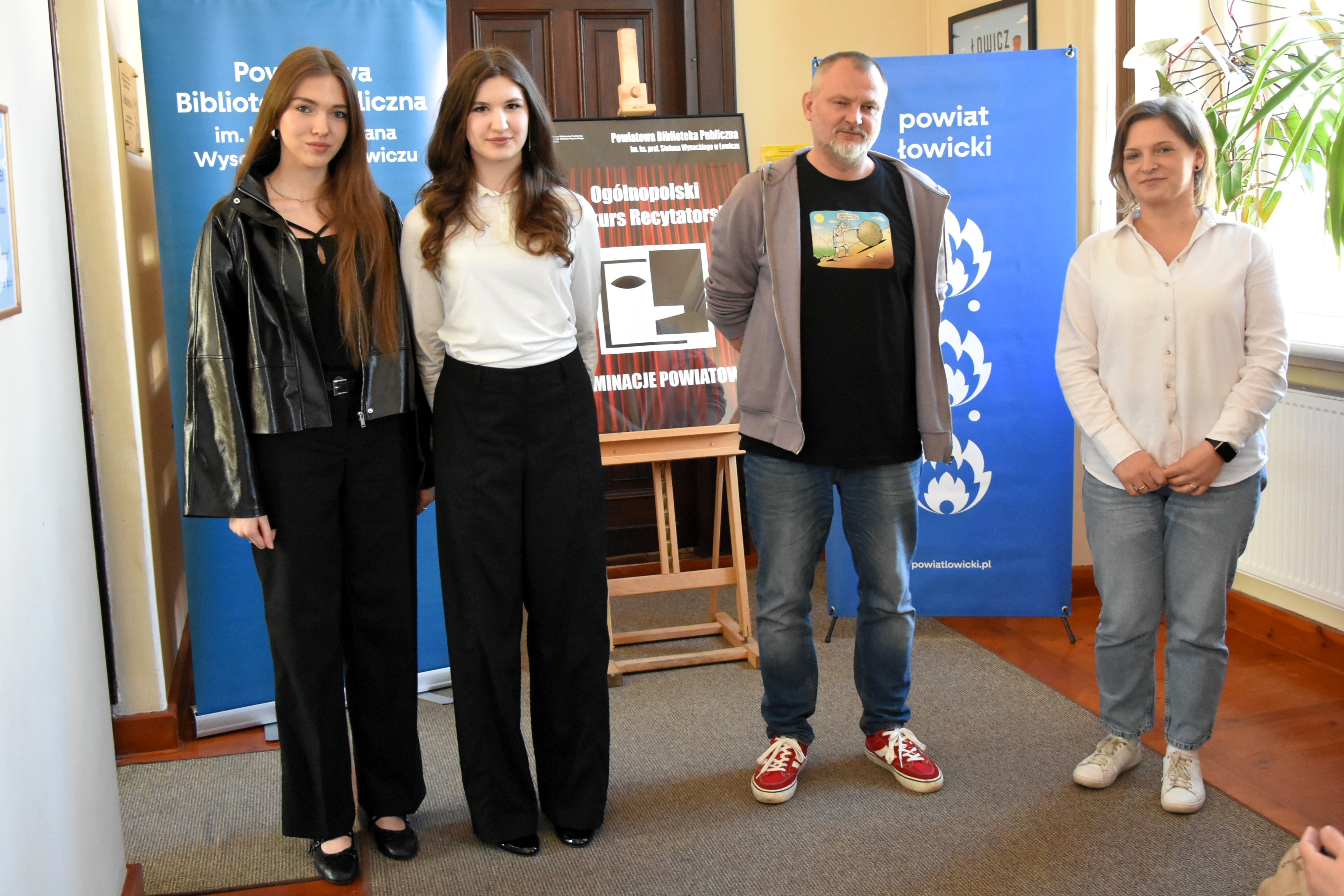 Trzy kobiety oraz mężczyzna pozują do zdjęcia na tle banerów oraz plakatu.